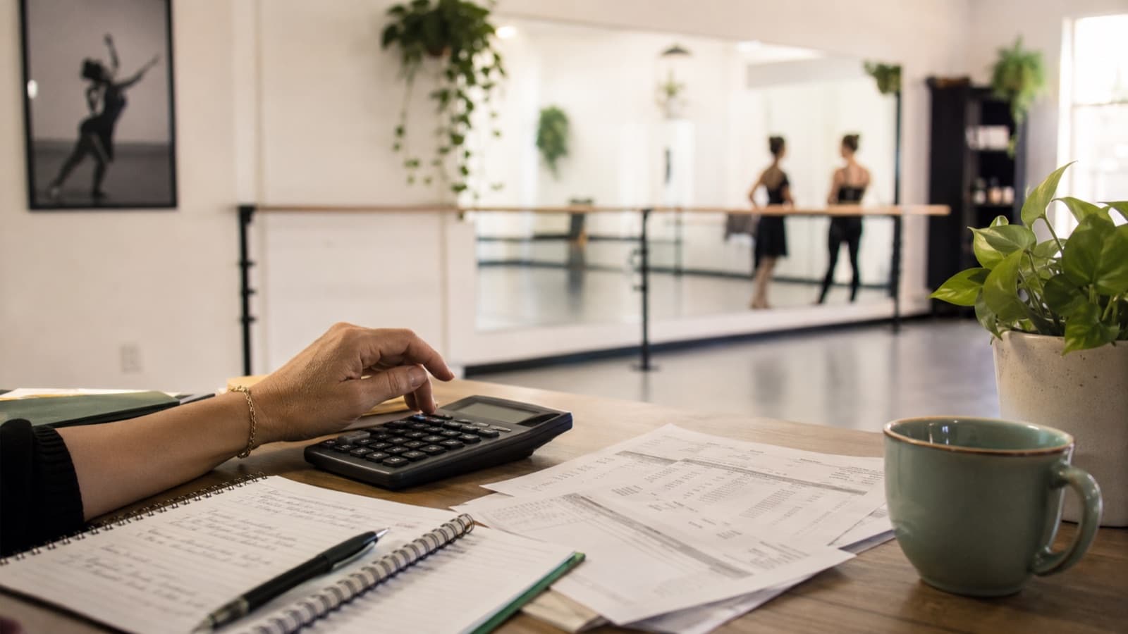 Mesa com notas, calculadora e planilha financeira de uma escola de dança