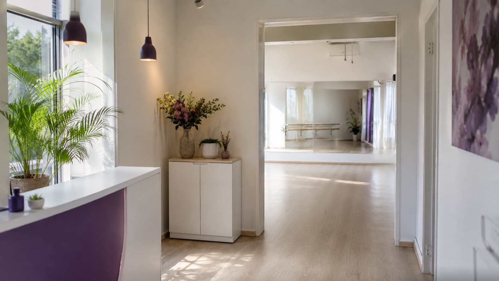 Recepção limpa e acolhedora de uma escola de dança com espelhos e piso da sala ao fundo